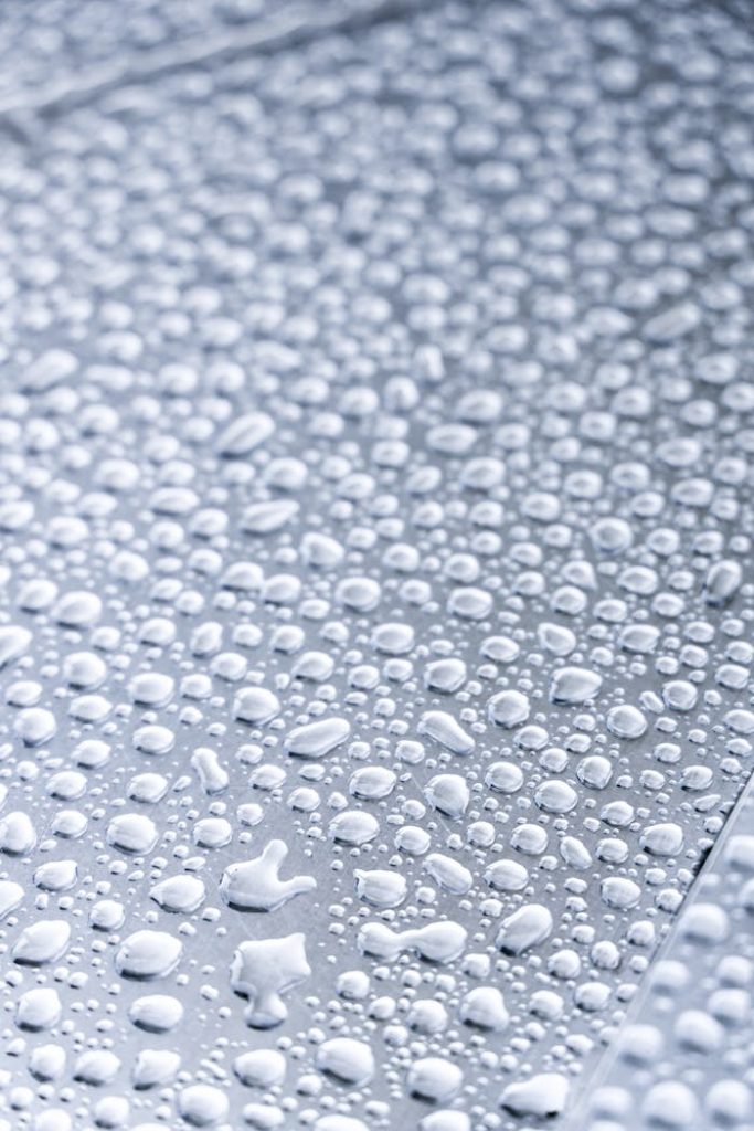Detailed macro shot of water droplets on a metallic surface, highlighting texture and reflection.