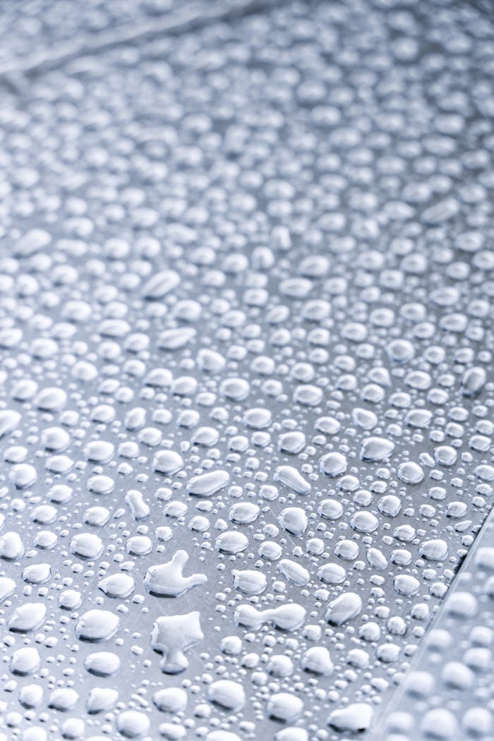 Detailed macro shot of water droplets on a metallic surface, highlighting texture and reflection.