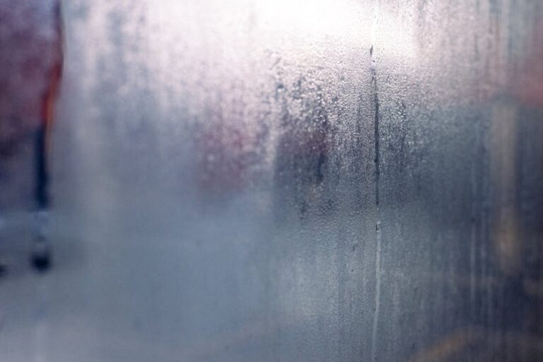 Moisture droplets on a foggy window create a mysterious and serene atmosphere.