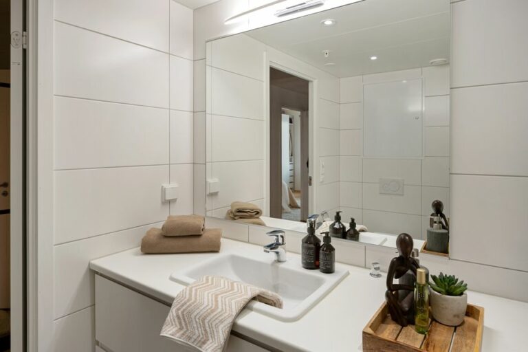 Elegant modern bathroom with white tiles, large mirror, and stylish accessories like towels and toiletries enhancing the decor.